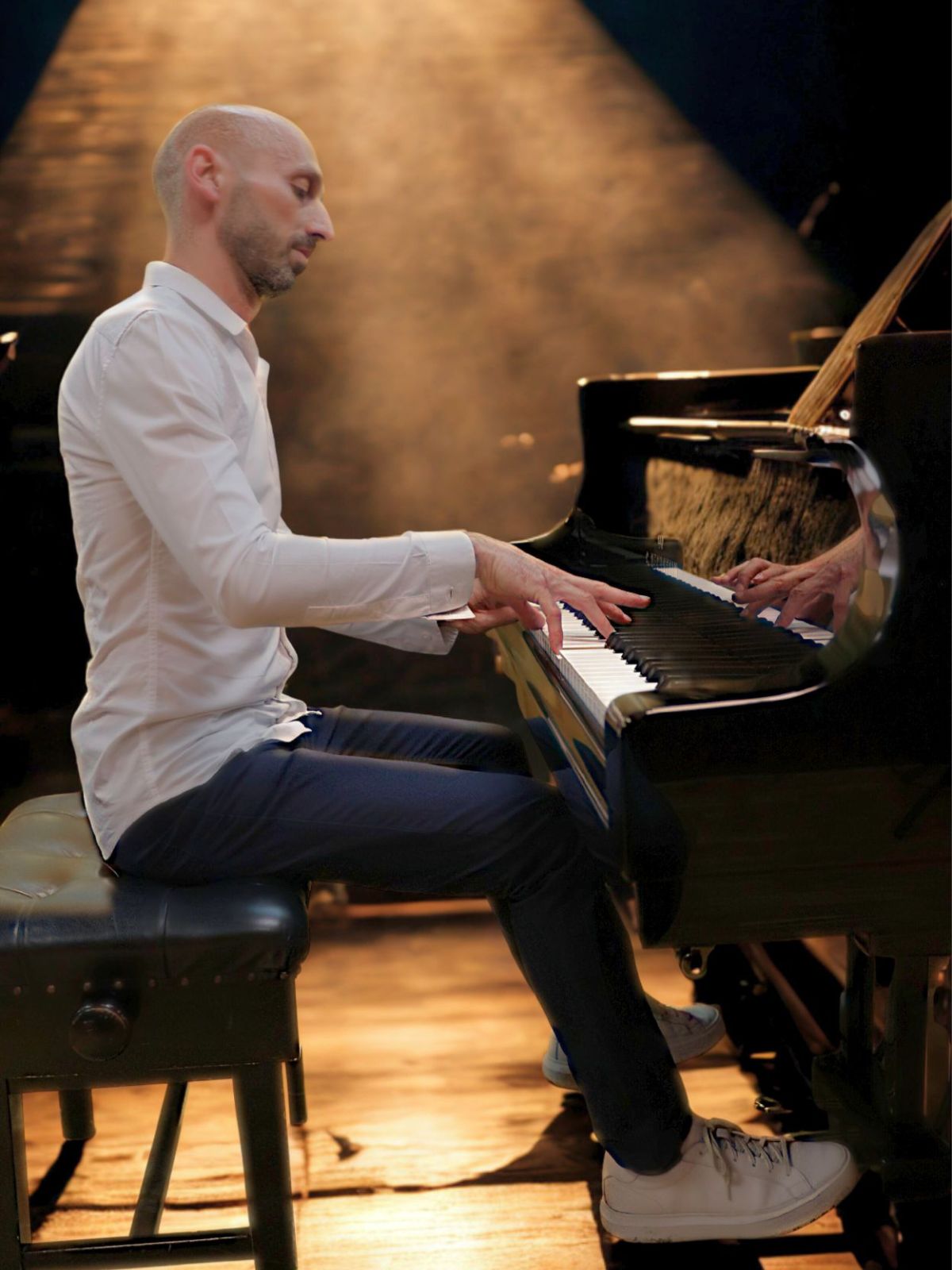 Pianist Tim Dimov performing at grand piano under warm spotlight