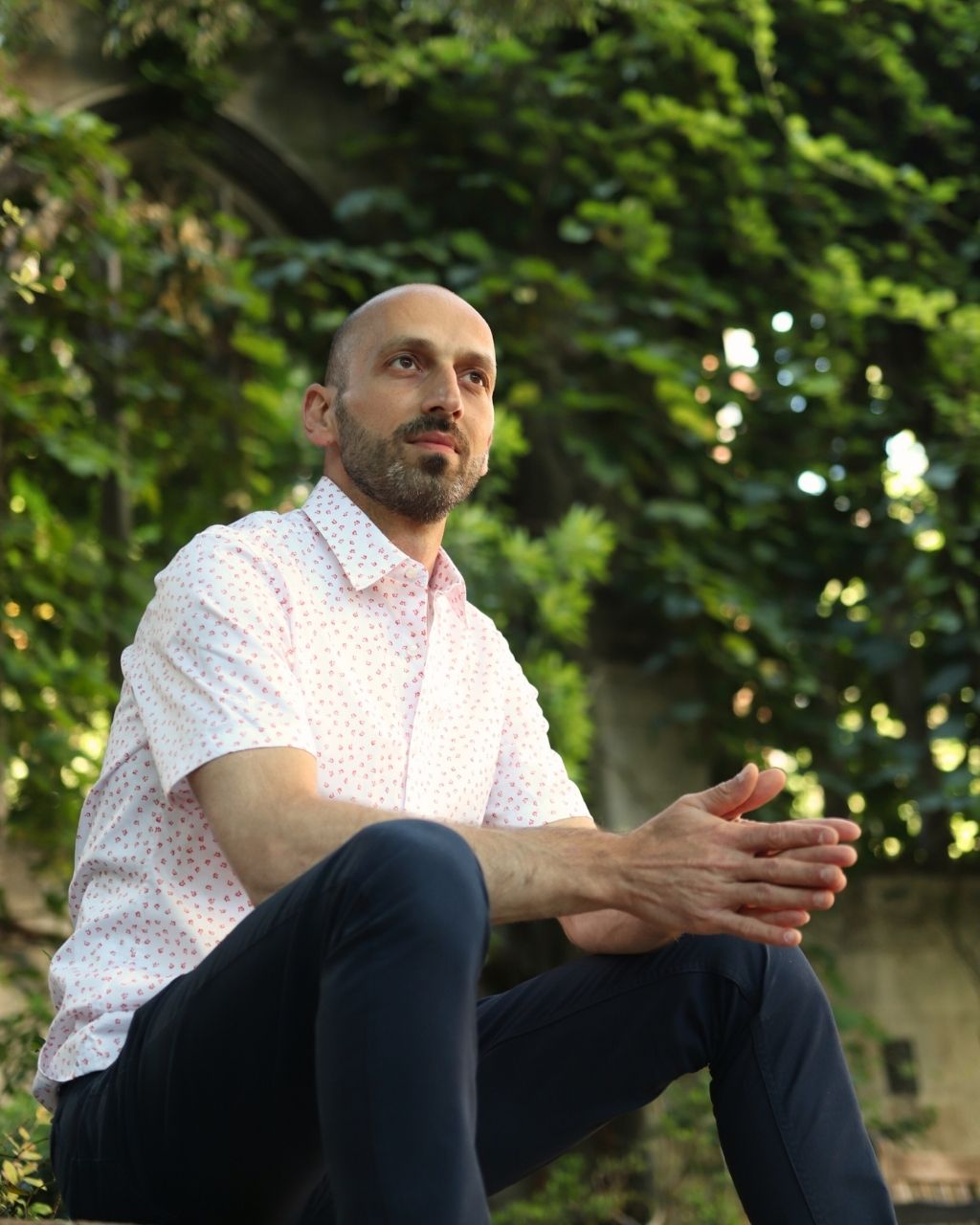 Tim Dimov seated in a leafy courtyard, thoughtful and calm.